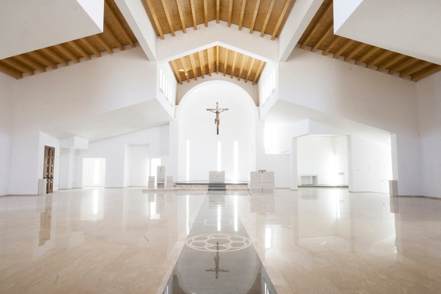 Un tappeto intarsiato in marmo conduce al presbiterio, volumi bianchi, luce, copertura in legno | arch. Benedetta Fontana