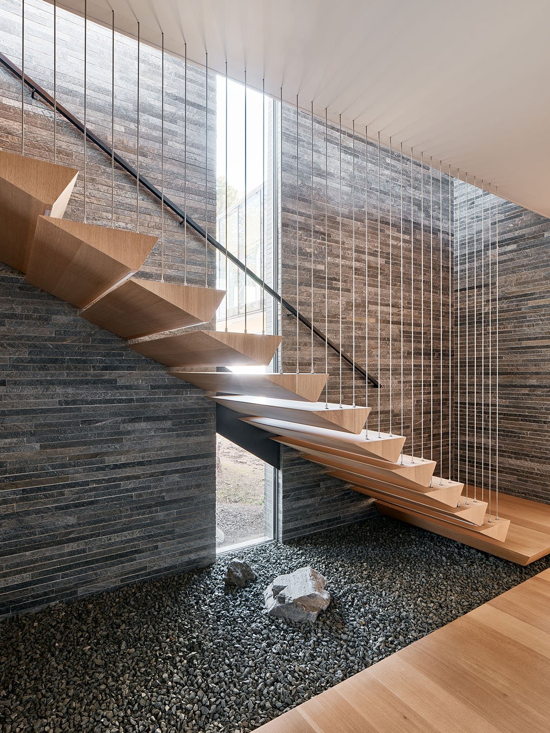 Natural stone textures ground the elegantly suspended stairway that connects the main living spaces to bedrooms. | Joe Fletcher