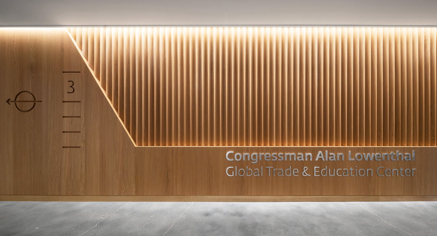 Step into the sophisticated elevator lobby featuring elegant triangular fluted wood slats in a warm wood veneer to create a welcoming and refined experience. The subtle lighting enhances the natural texture of the wood, guiding visitors into a space desig | Paul Vu