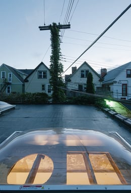 Photograph showing a view taken from the roof, looking across one of the new domed skylights with the "his and hers" cutouts, into the residential neighborhood. Though the building typology differs so much | Florian Holzherr