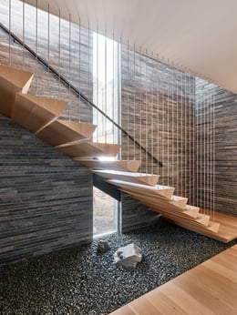 Natural stone textures ground the elegantly suspended stairway that connects the main living spaces to bedrooms. | Joe Fletcher